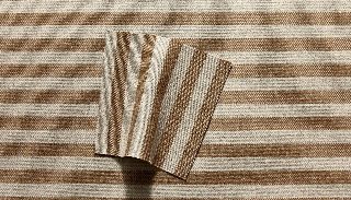 Camira Monochrome Sett II kumaşının taba ve krem tonlarında iri çizgi deseninin yakın çekimi, ince çizgili arka yüzü kıvrılmış halde