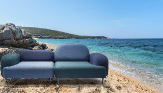 Camira Oceanic kumaşıyla döşenmiş gri mavi, lacivert ve yeşil modüler kanepe, turkuaz deniz ve kayalık sahil önünde