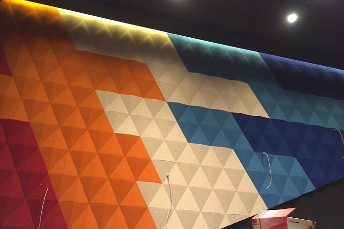 Etkinlik salonu duvarında turuncudan maviye geçiş yapan üçgen piramit yüzeyli 3D akustik panel kaplama