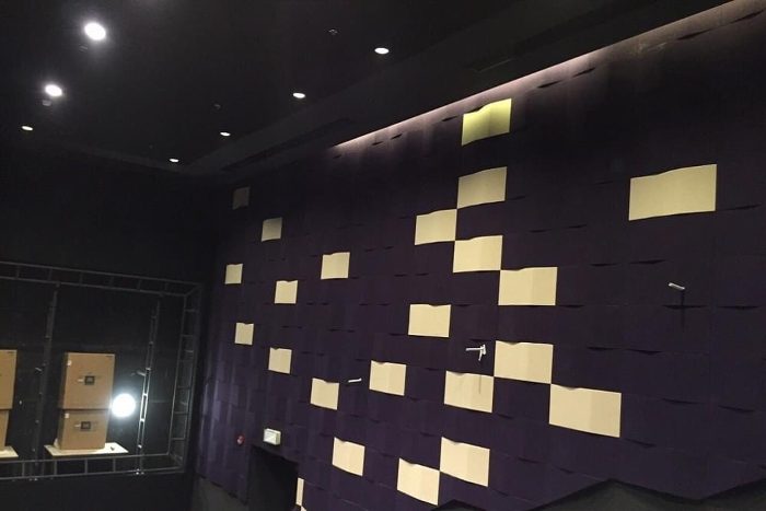 Loş sinema salonunda mor zemin üzerine krem detaylı dalga yüzeyli akustik duvar paneli kaplaması