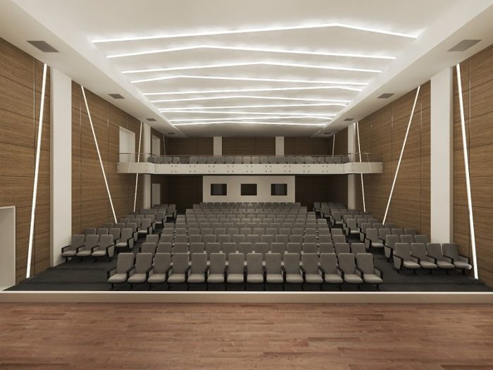 Konferans salonunda duvarları kaplayan koyu ceviz tonlu ahşap akustik panel ve gri koltuklar