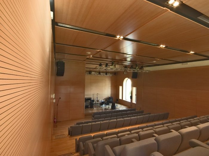 Çok amaçlı etkinlik salonunda sahne ve duvarlarda kanal desenli akustik ahşap duvar paneli