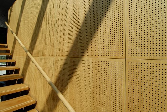 Merdiven boşluğu duvarını kaplayan açık meşe tonlu delikli ahşap akustik panel uygulaması