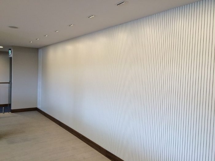 Ofis koridorunda beyaz yüzeyli ince çıtalı ahşap akustik panel ile kaplanmış geniş duvar