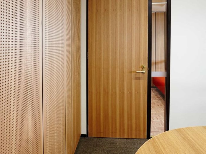 Ofis girişinde delikli ahşap akustik panel kaplı duvarlar ve meşe kaplama kapı detayı