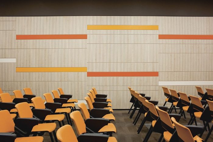Seminer salonu duvarında turuncu ve sarı bantlı krem tonlu çıtalı ahşap akustik panel