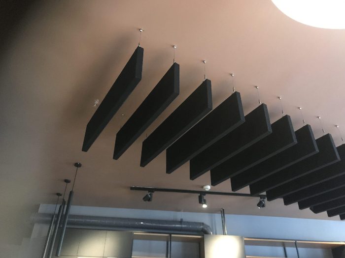 Renkli duvara askı halatlarıyla monte edilmiş siyah akustik baffle panel sırası