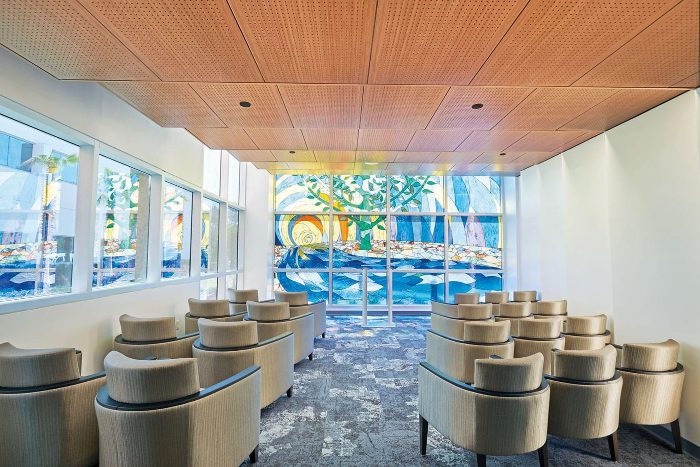 Delikli ahşap panel tavanlı bekleme salonu, vitray pencere ve bej koltuklar