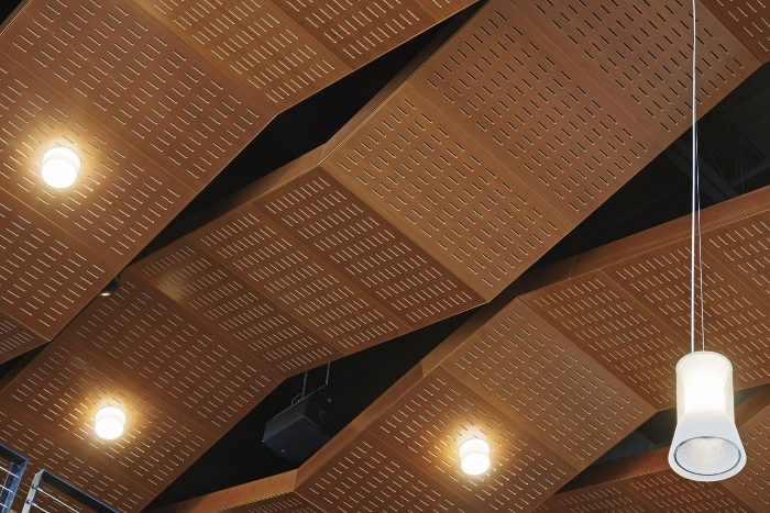 Sıralı kısa yarıklı ceviz tonlu akustik tavan panelleri, üçgen açılı kanopi düzeni ve sarkıt aydınlatma
