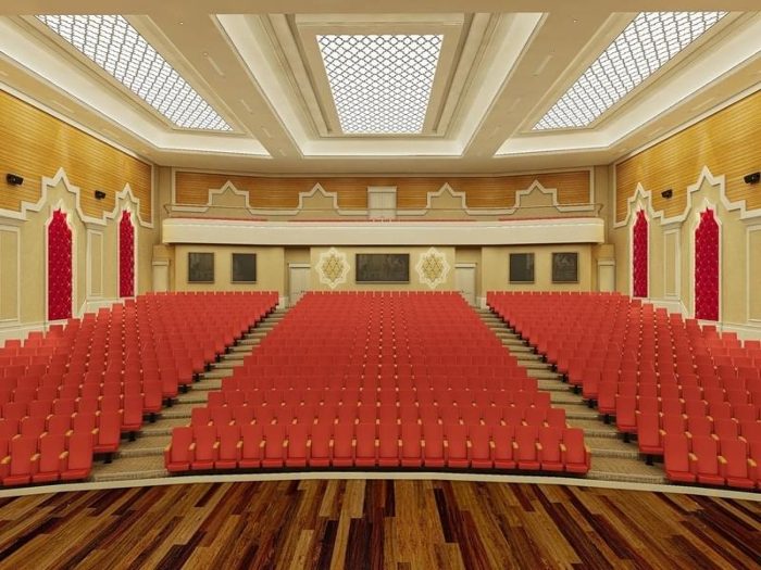 Oditoryum renderı, yan duvarlarda ahşap derzli akustik panel, kırmızı koltuklar ve ahşap sahne zemini