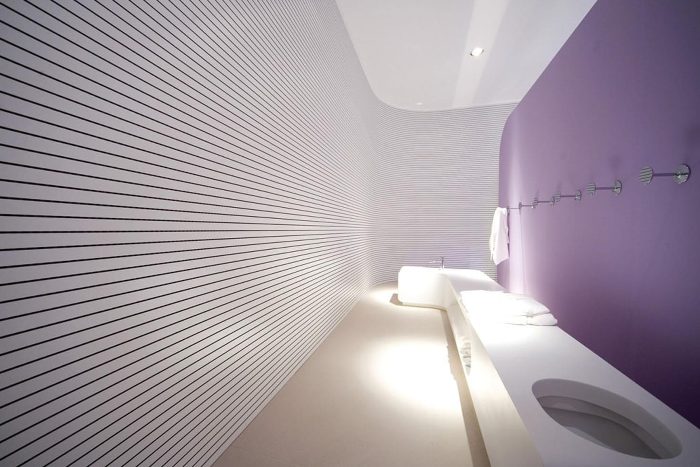 Otel banyosunda beyaz yatay ince derzli akustik duvar paneli, mor duvar ve beyaz lavabo