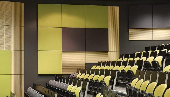 Ders salonu duvarında yeşil tonlarda kumaş kaplı akustik panel ve ahşap lamel kompozisyonu