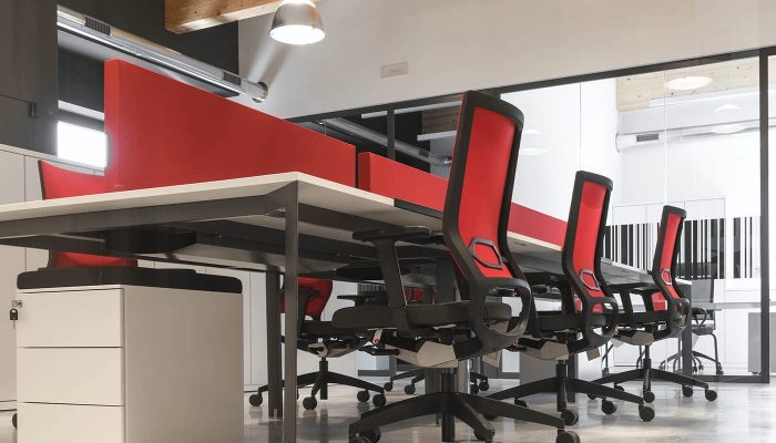 Açık ofiste bench masaları bölen kırmızı emici masa ekranları ve sıralı çalışma koltukları