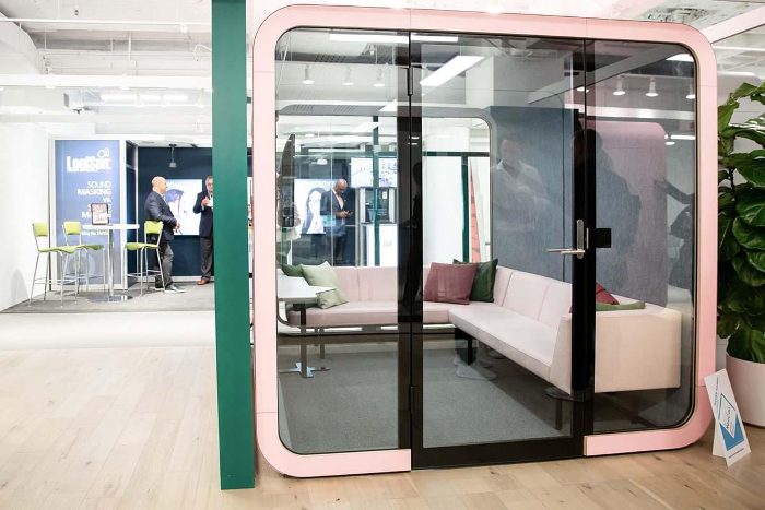 Akustik toplantı kabini pudra pembesi model, showroom ortamında beyaz koltuklu lounge düzeni