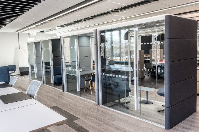 Bağımsız ofis bölümü antrasit kumaş panelli kabin sırası, katlanır cam kapıları ve ahşap zeminli açık ofis koridoruyla