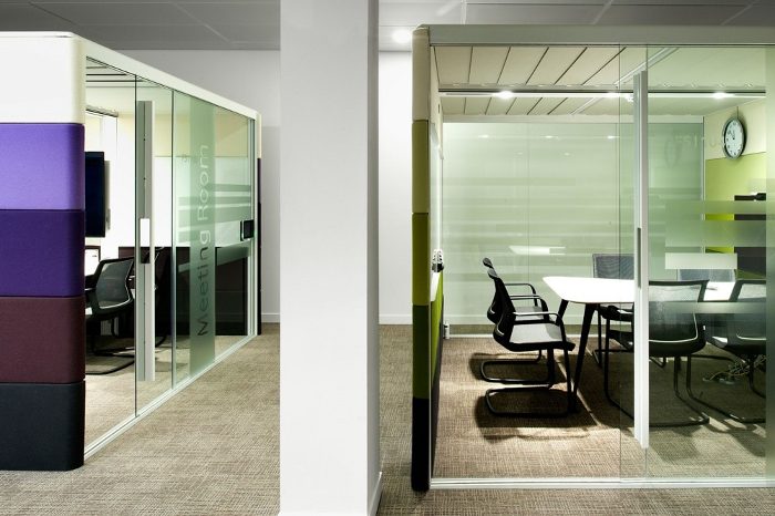 Bağımsız ofis bölümü mor panelli Meeting Room kabini ile yeşil panelli cam toplantı odası, siyah sandalyeler ve duvar saatiyle