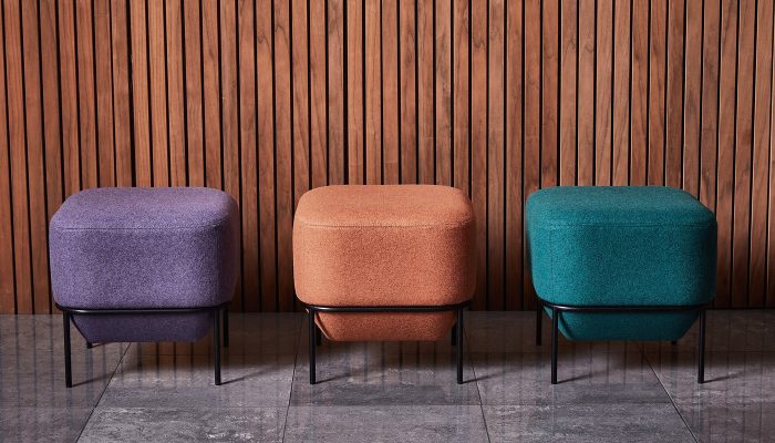 Camira Blazer yün kumaşıyla döşenmiş mor, kiremit ve petrol yeşili üç oturma pufu, ahşap latalı duvar önünde