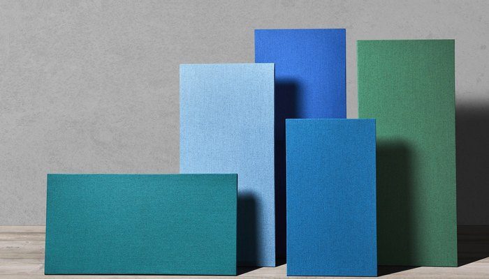 Camira Blazer Lite yün kumaşıyla kaplı beş akustik panel, petrol, mavi ve yeşil tonlarda ahşap zemin üzerinde