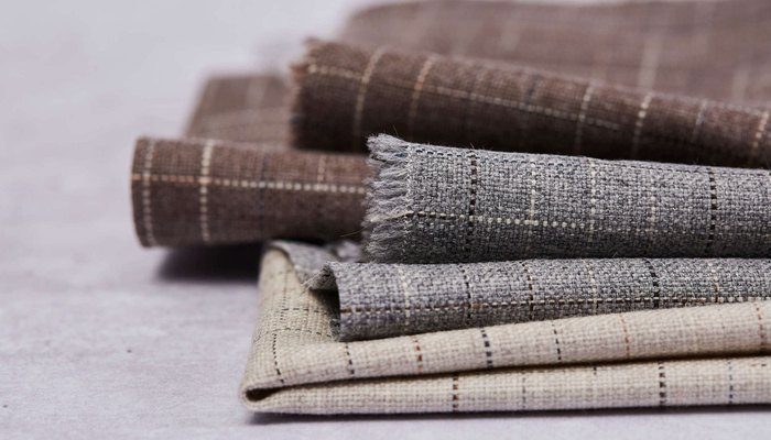 Camira Kyoto yün kumaşının kahve, gri ve krem tonlarında ince ızgara desenli ruloları, açık zeminde