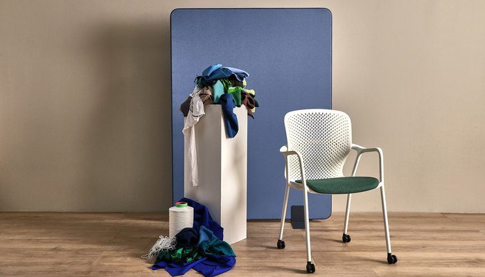 Camira Lucia T2T kumaşıyla kaplı mavi akustik paravan, yanında beyaz sandalye, kumaş atıkları ve iplik bobiniyle geri dönüşüm anlatısı