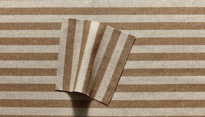 Camira Monochrome Sett II kumaşının taba ve krem tonlarında iri çizgi deseninin yakın çekimi, ince çizgili arka yüzü kıvrılmış halde