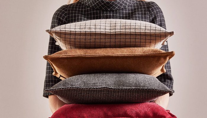 Camira Monochrome Sett kumaşıyla kaplı ızgara ve dokuma desenli yastıklar, taba ve kırmızı düz minderlerle bir kişinin kucağında