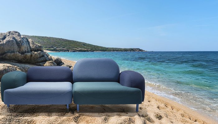 Camira Oceanic kumaşıyla döşenmiş gri mavi, lacivert ve yeşil modüler kanepe, turkuaz deniz ve kayalık sahil önünde