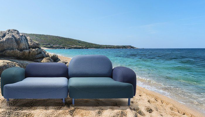 Camira Oceanic kumaşıyla döşenmiş gri mavi, lacivert ve yeşil modüler kanepe, turkuaz deniz ve kayalık sahil önünde