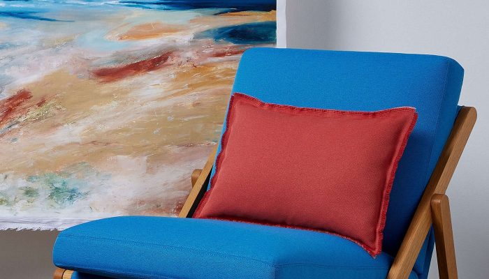 Camira Quest mavi kumaşıyla döşenmiş ahşap katlanır koltuk, kiremit rengi minder ve deniz manzaralı tabloyla