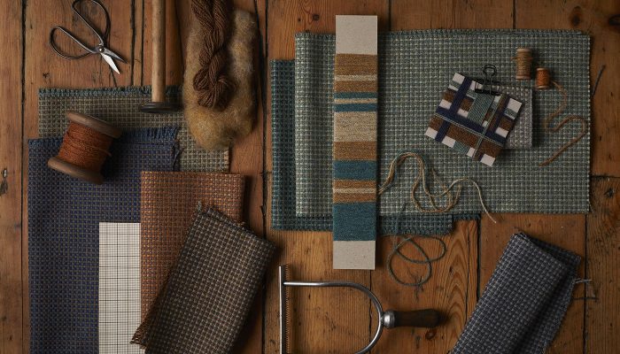 Camira ReSKU 2.0 kumaş örnekleri ahşap zeminde eski dokuma bobinleri, iplik çilesi, makas ve dokuma aletleriyle craft düzeninde