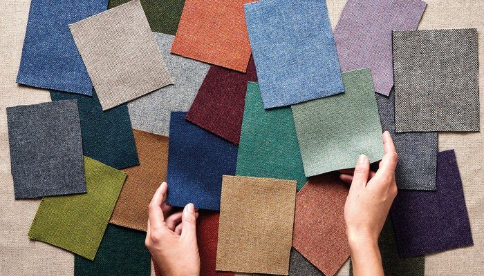 Camira Main Line Flax yün ve keten kumaşının mavi, yeşil, mercan, mor ve toprak tonlardaki çok sayıda örneği, keten zemin üzerinde ellerle düzenlenirken