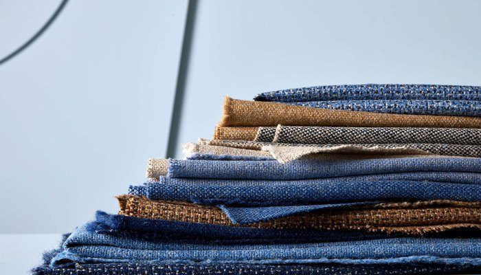 Camira Main Line Twist yün ve keten kumaşının büküm iplikli dokusu, denim mavisi ve taba tonlarda katlı yığın halinde