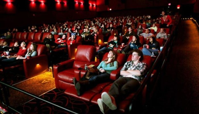 Dolu bir sinema salonunda kırmızı koltuklarda oturan seyirciler