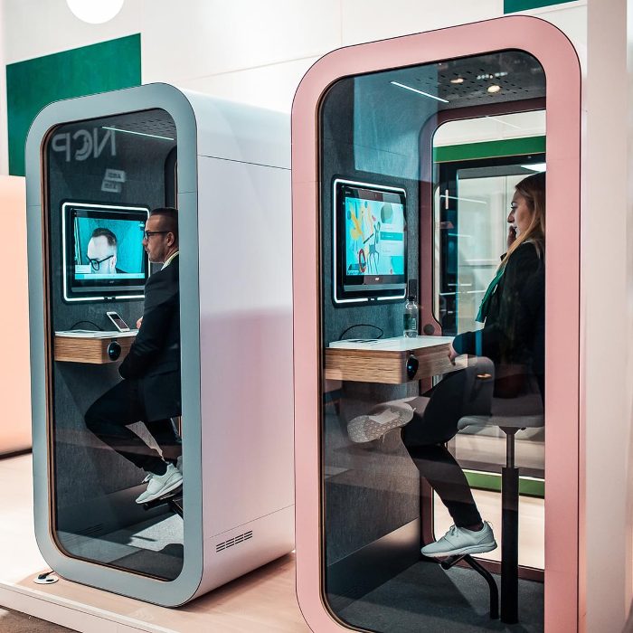 Telefon görüşme kabini gri mavi ve pudra pembe çerçeveli iki modeliyle showroomda, içlerinde ekran karşısında görüşme yapan kullanıcılar