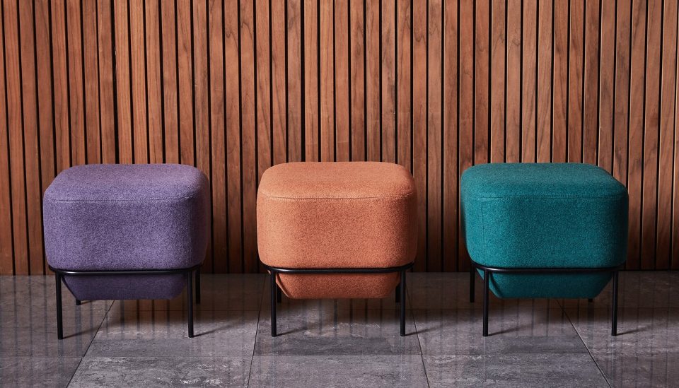 Camira Blazer yün kumaşıyla döşenmiş mor, kiremit ve petrol yeşili üç oturma pufu, ahşap latalı duvar önünde