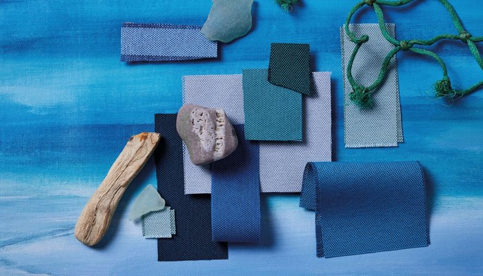 Camira Quest kumaşının mavi tonlardaki örnekleri, deniz camı, deniz odunu ve yeşil balık ağıyla okyanus temalı kompozisyonda
